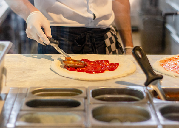 Cook spreading red sauce on pizza crust