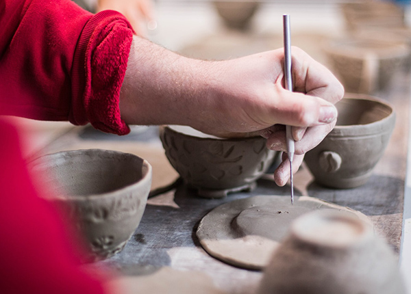 Woman carving floral designs into clay bowls