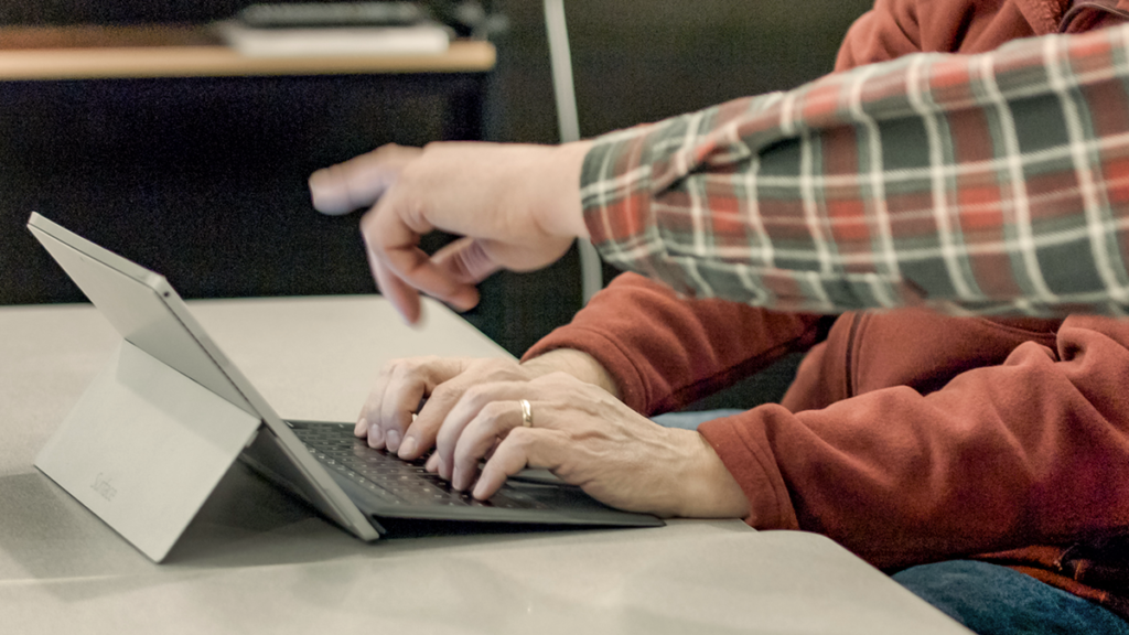 One person types on a laptop as another person points at the screen