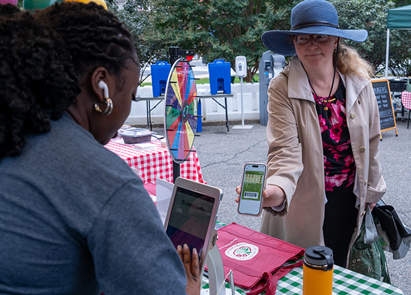 Woman holding a phone while making a purchase at a vendor stand in a market