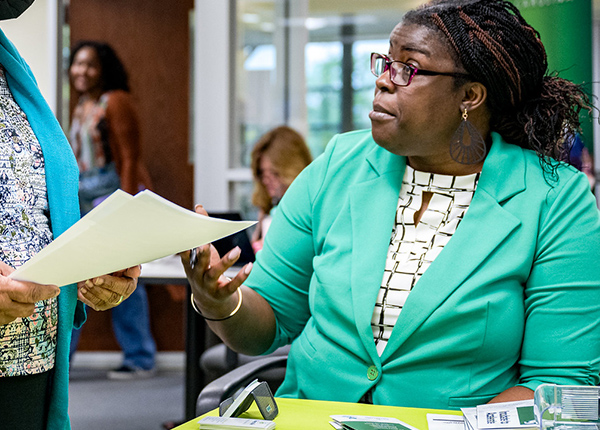 Woman talks to another woman who is holding a small stack of papers