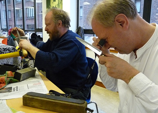 Two men sharpening blades at an event
