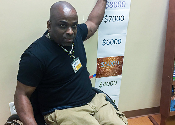 Man who uses a wheelchair displaying a fundraising chart on the wall