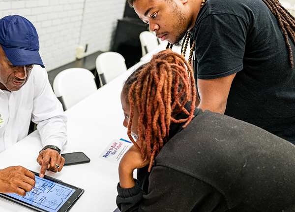 Three people around a table looking at a digital tablet