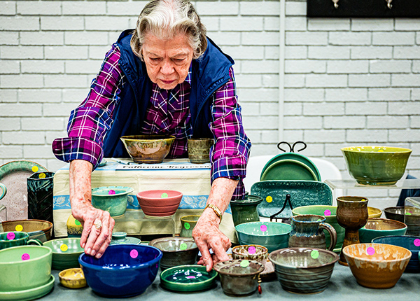 Woman leaning over arranging bowls for display at a craft fair