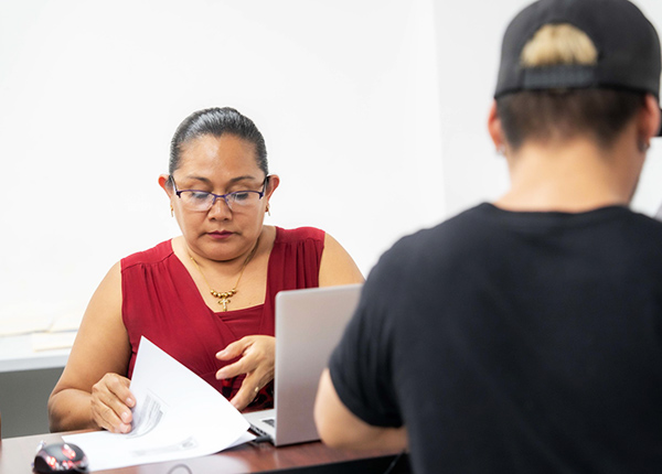 Woman sitting across a desk from someone flipping through papers next to a laptop