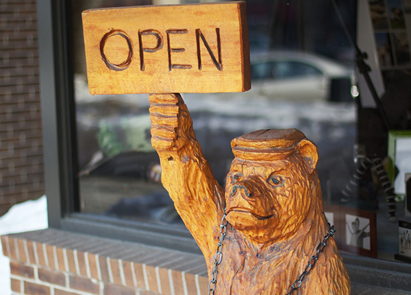Carved wooden bear holding an Open sign outside of a business