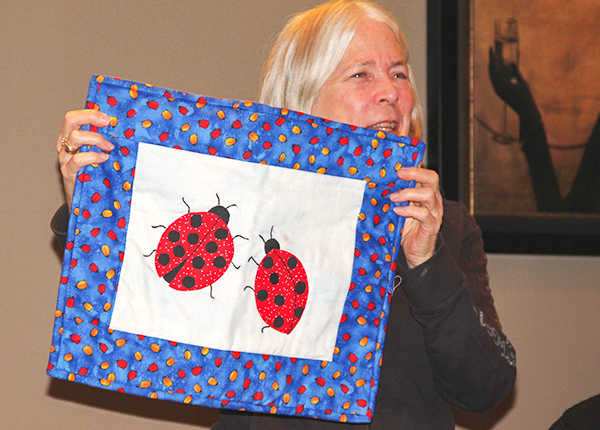 Woman holding up quilt square with two ladybugs on it
