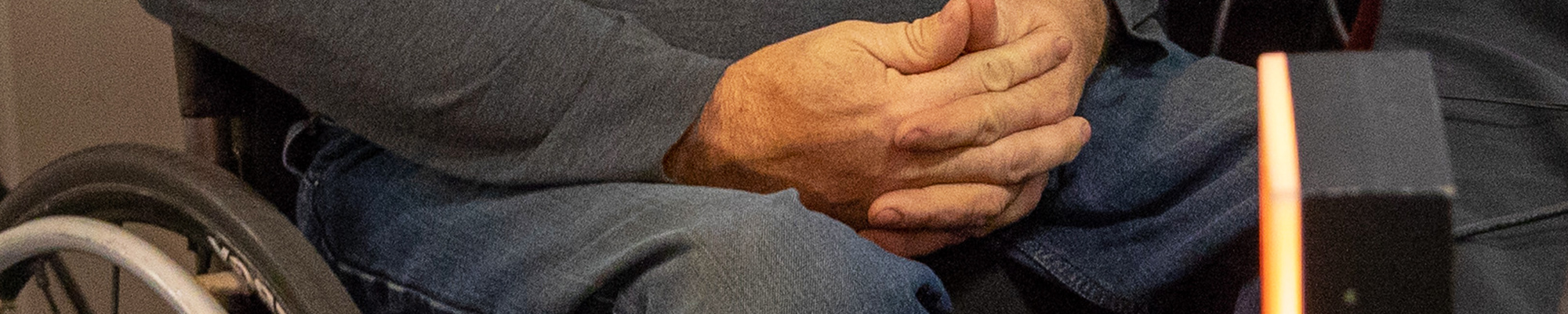 Banner image: Close-up of a person who uses a wheelchair with clasped hands resting in their lap