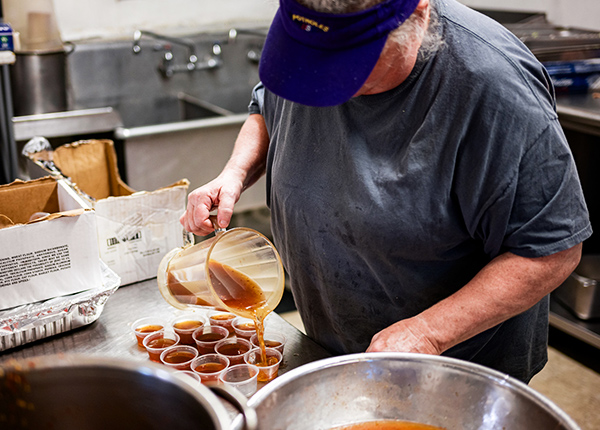 Person pouring a pitcher of barbecue sauce into small containers