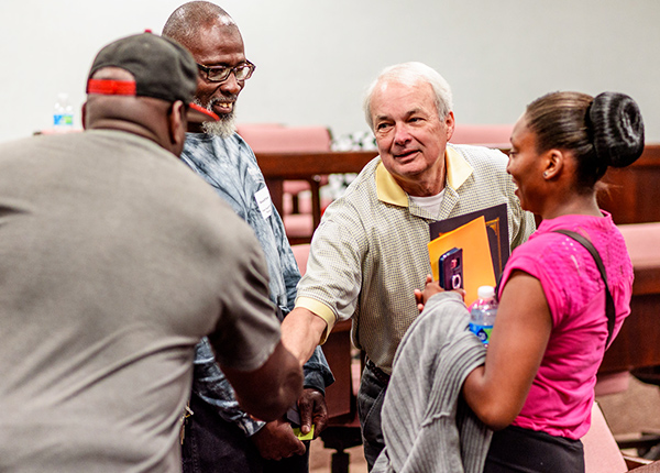 A small group of people standing in a circle while two shake hands