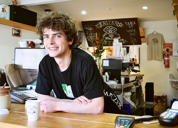 Young man working at a coffee shop smiling and leaning over the counter
