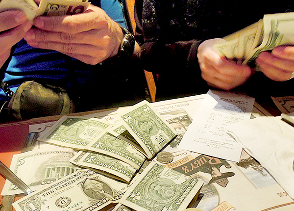 Two people sitting at a table counting a pile of cash