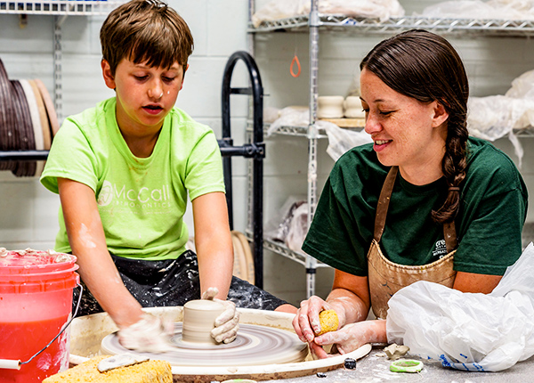 A woman showing a young boy how to use a pottery wheel