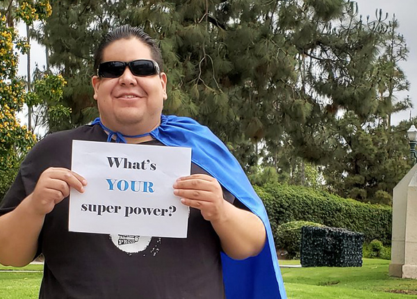 Man wearing a cape with a sign that says What's your super power?