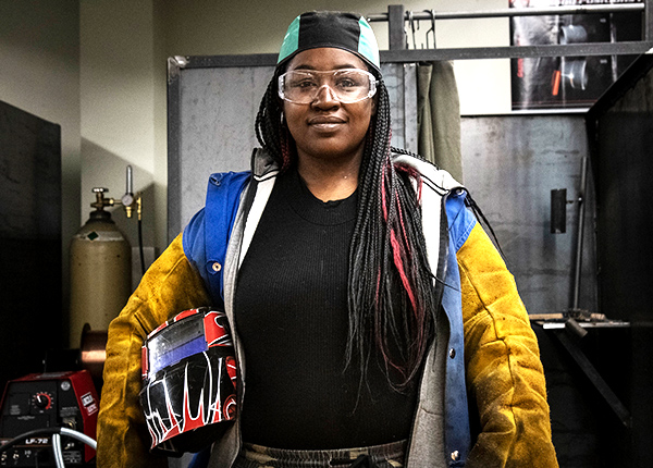 Woman smiling at the camera and holding welding gear