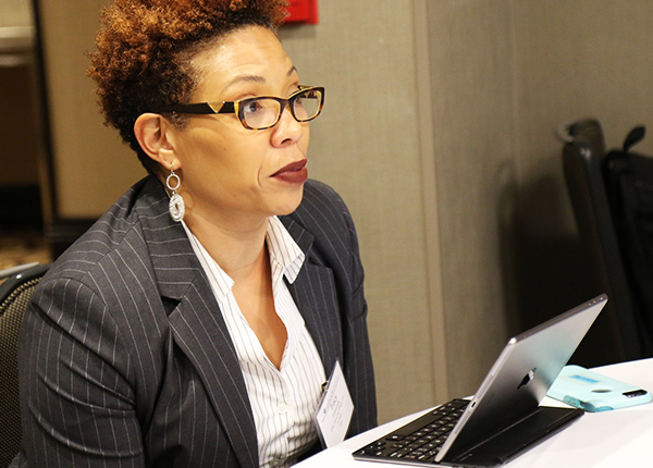 Woman in business attire sitting at a table with a digital tablet in front of her
