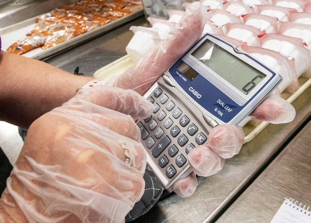 Person wearing serving gloves while punching numbers into a calculator