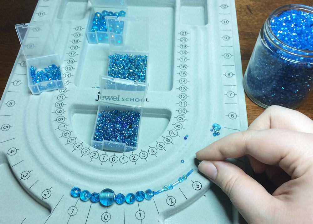 Person putting beads into a plastic tool used to make necklaces