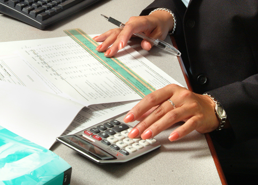 Person using a ruler on a printed spreadsheet and using a calculator with their other hand