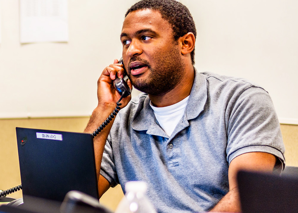 Man sitting behind a laptop and talking on the phone
