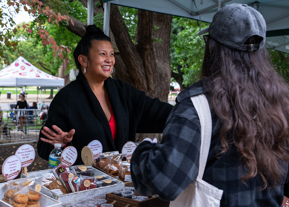 Woman selling baked goods talking to a customer at a vendor stand