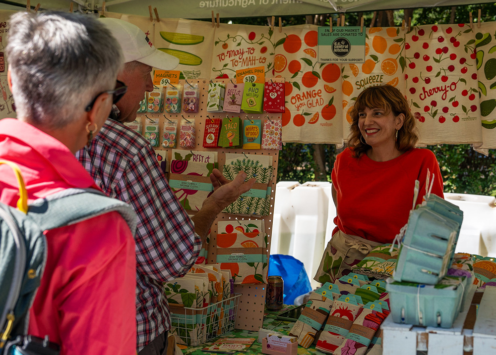 Woman selling seeds and tea towels at a vendor stand chats with customers