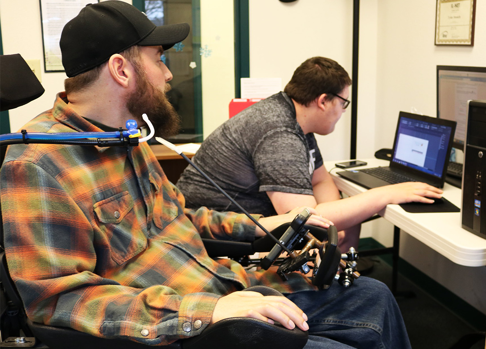 Two people, one who uses a wheelchair, looking at something on a laptop screen