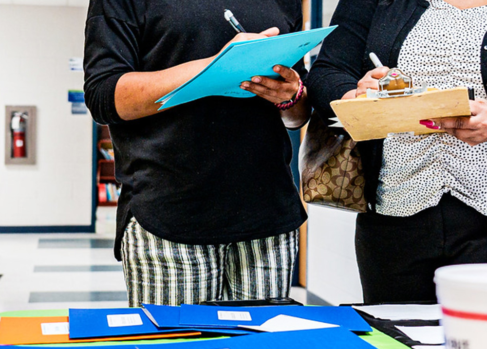 Two people standing next to each other holding clipboards and writing on them