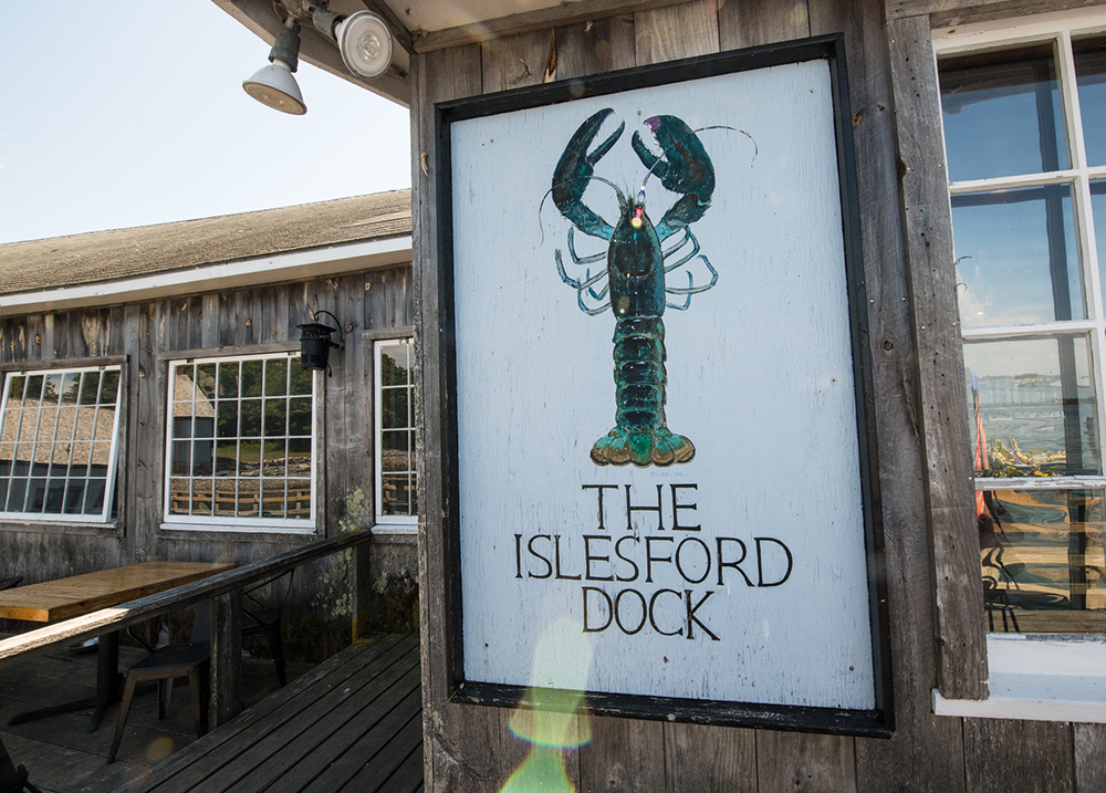 A sign with a lobster on it that says The Islesford Dock on a rustic building