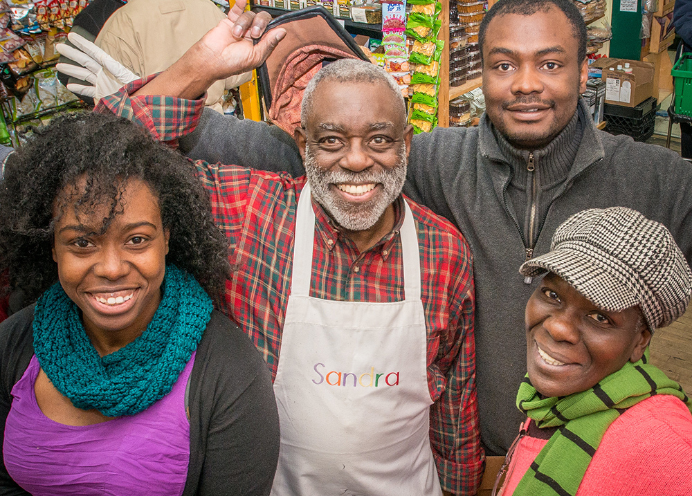 Older man wearing an apron smiles for a photo with three younger people