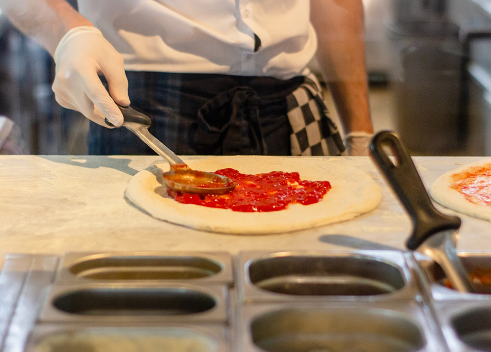 Person spreads sauce on pizza dough