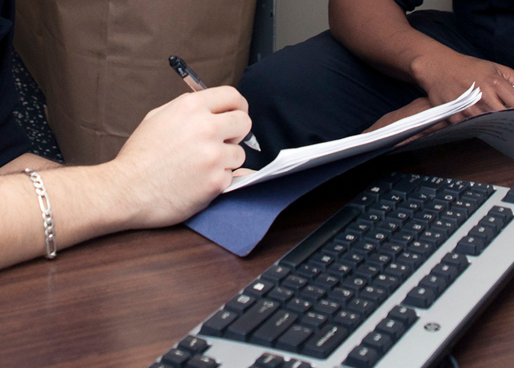 Hand holding a pen near a stack of papers in front of a computer keyboard