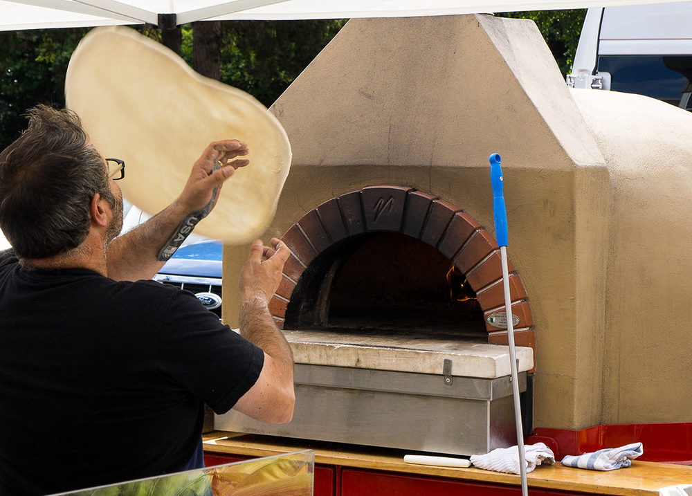 Man tossing pizza dough in front of a pizza oven