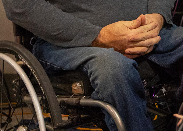Close-up of a person who uses a wheelchair with clasped hands resting in their lap