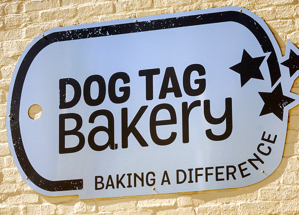 Sign on a wall that says Dog Tag Bakery - Baking a Difference