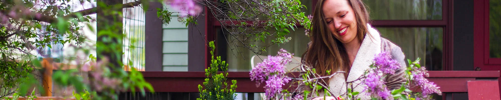 Woman standing behind a lilac bush smiling