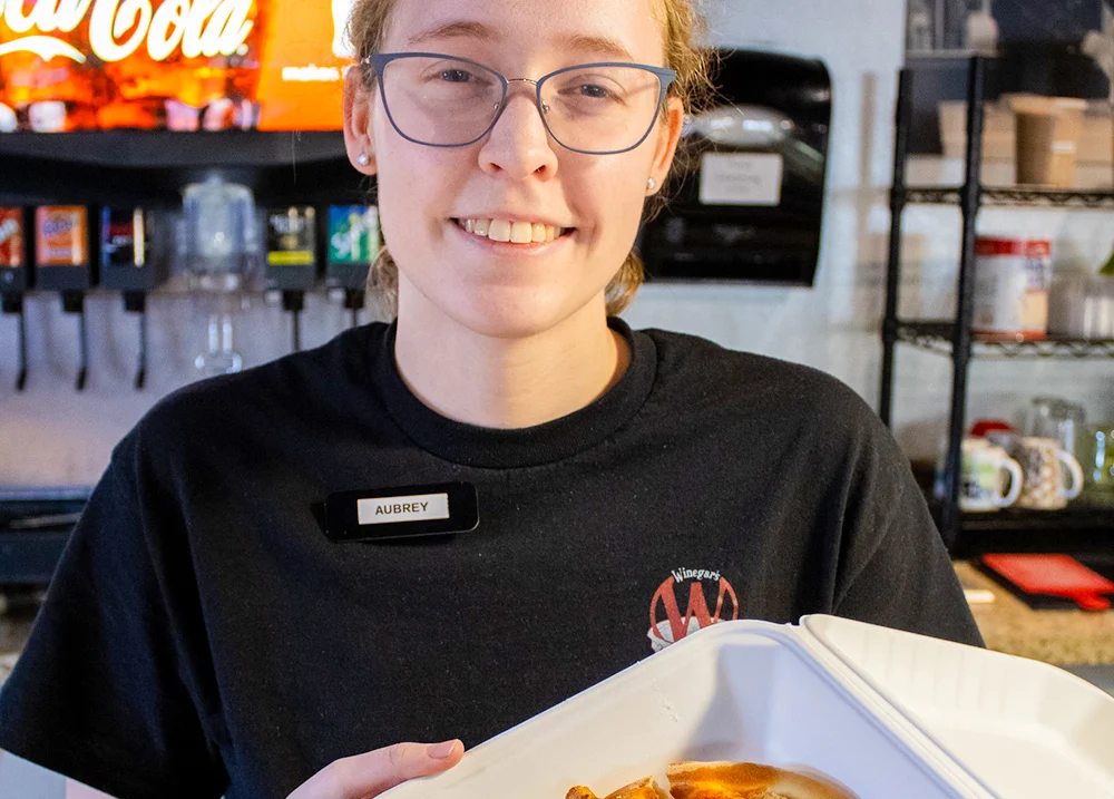 Worker holding a box of pizza and smiling