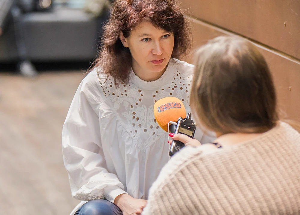 Two people sit together doing an interview, one holds a microphone