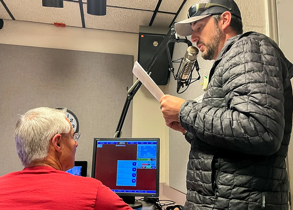Man at a recording studio reading from a script and speaking into a microphone