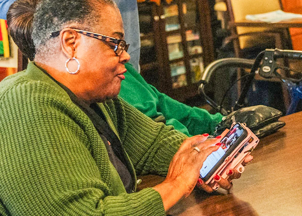 Woman sits at a table and taps on her cell phone screen