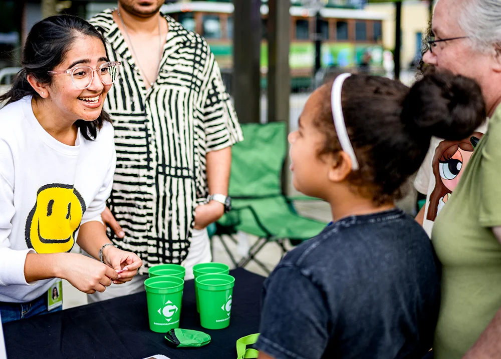 Woman standing at a vendor table talking to a young girl