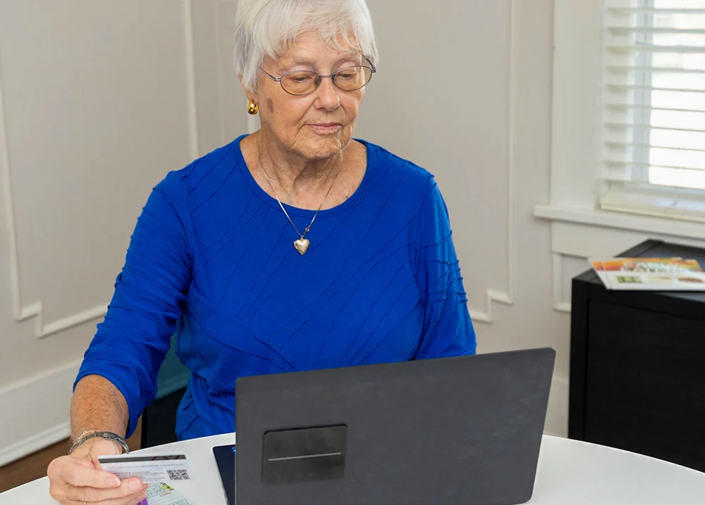 Woman looking at a laptop and holding a credit card in her hand next to the screen