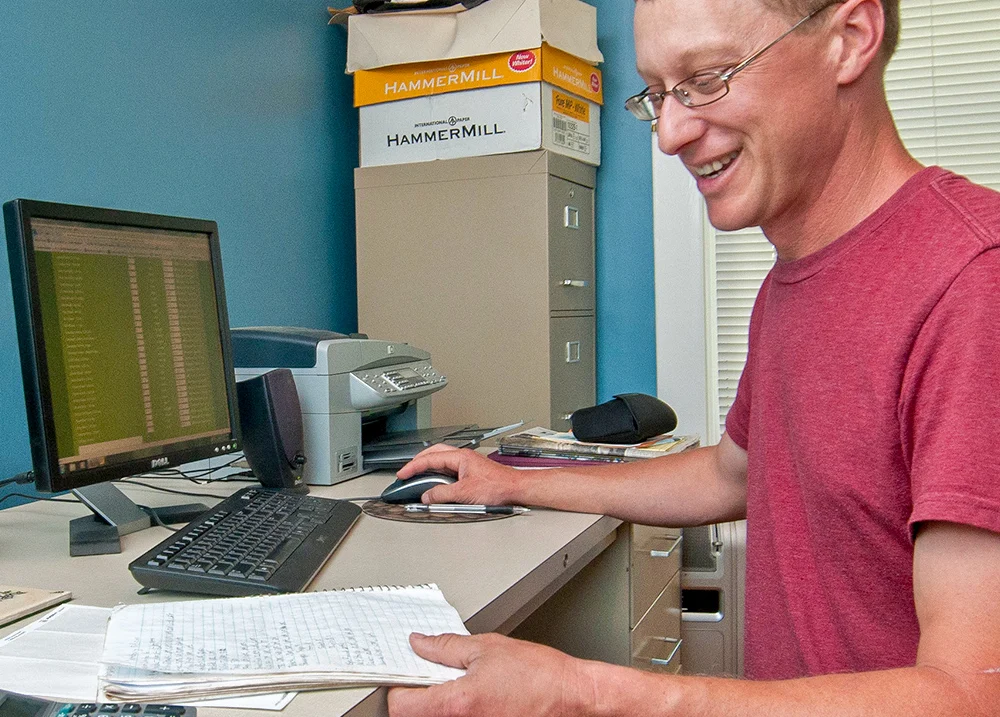 Man using a computer and looking at a notebook on his desk
