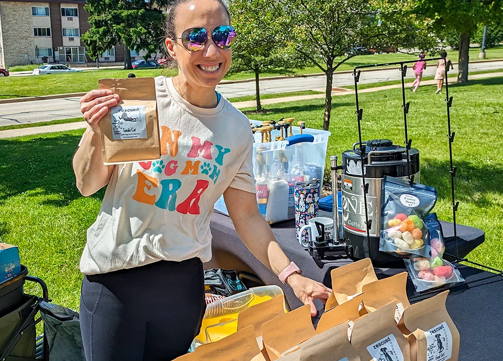 Woman at a vendor table holding a paper bag with a label on it