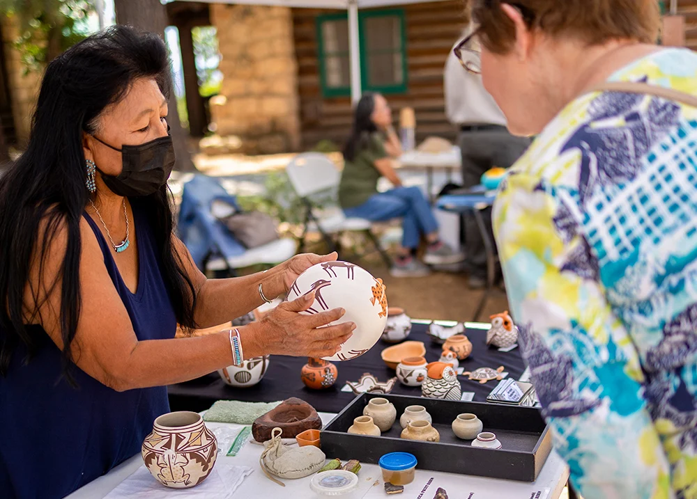 Woman holding a piece of pottery while a customer leans over the table to look at it