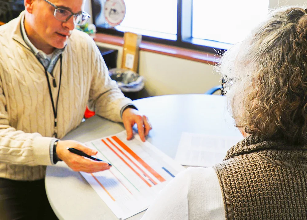 Two people sitting at a table looking at a printed spreadsheet