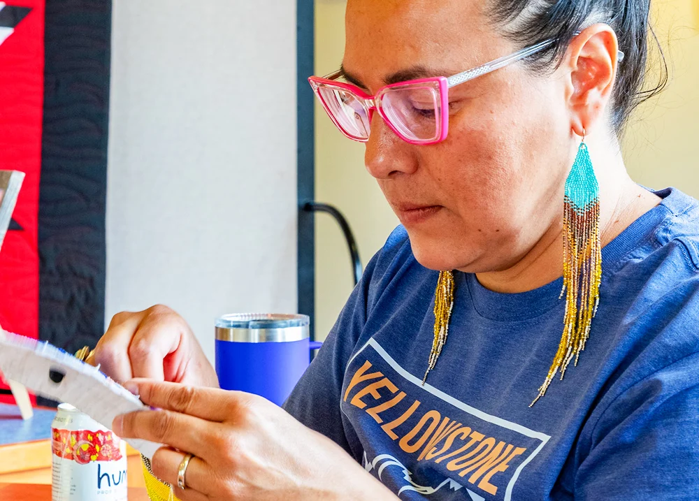 A woman with large, beaded earrings making some kind of craft