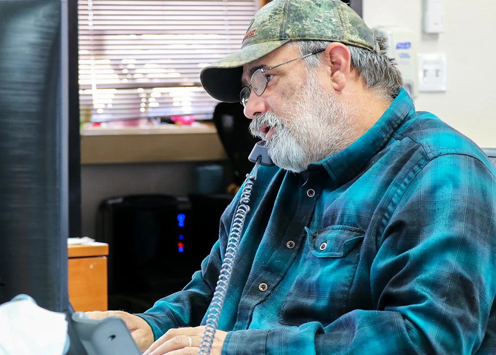 Man in front of a computer with a telephone between his shoulder and ear