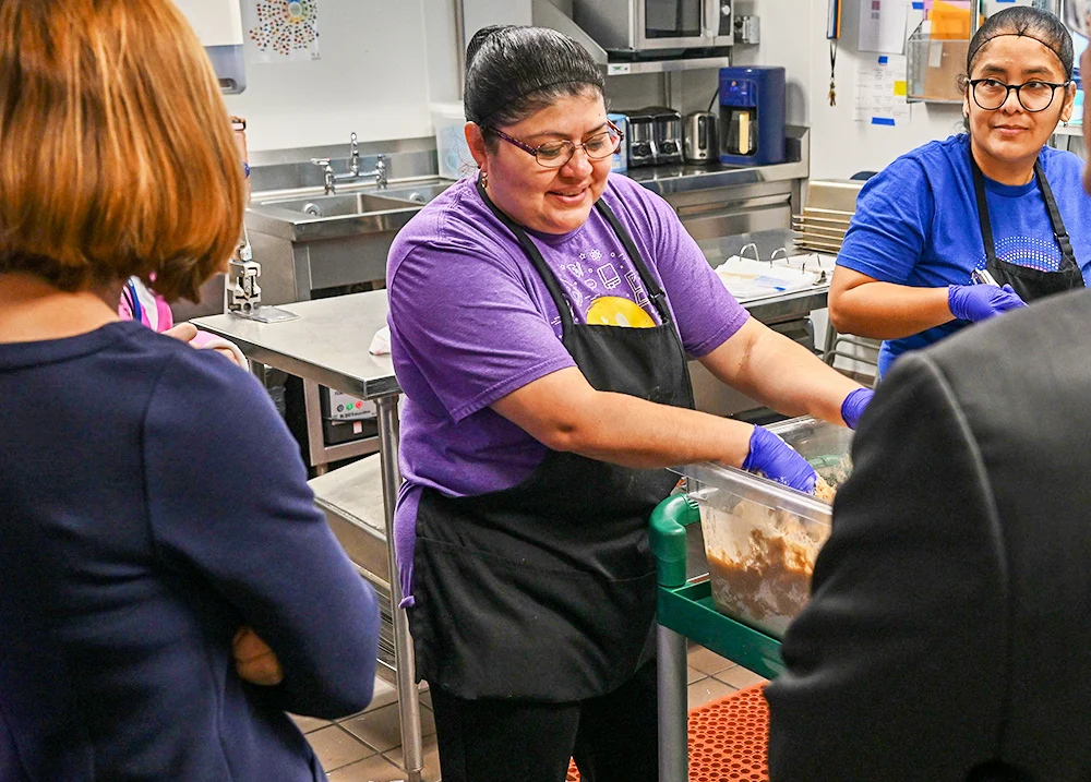 People inspecting two women who are working in an industrial kitchen